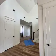 A bright, modern entryway with white walls, high ceilings, wood-look flooring, and closed white interior doors.