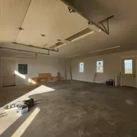 An unfinished garage interior with concrete floors, white walls, two windows, and overhead garage door tracks.