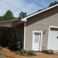 A beige house with a tan vinyl-sided garage, a white entry door, and a covered porch on a sunny day.