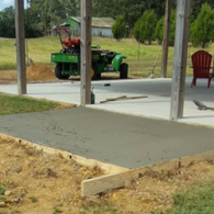A freshly poured concrete patio slab with wooden forms, situated under a covered porch area with a green utility vehicle.