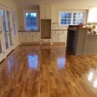 A high-angle view of a newly renovated kitchen with polished light hardwood floors, white cabinetry, and a kitchen island.