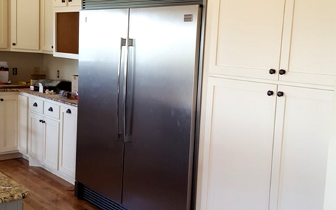 A large stainless steel refrigerator flanked by cream-colored cabinets in a kitchen.