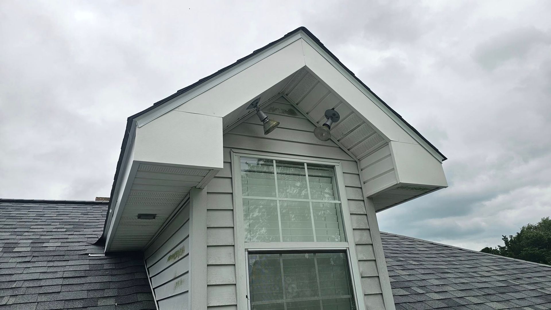 White dormer with window on a gray roof, under a cloudy sky.