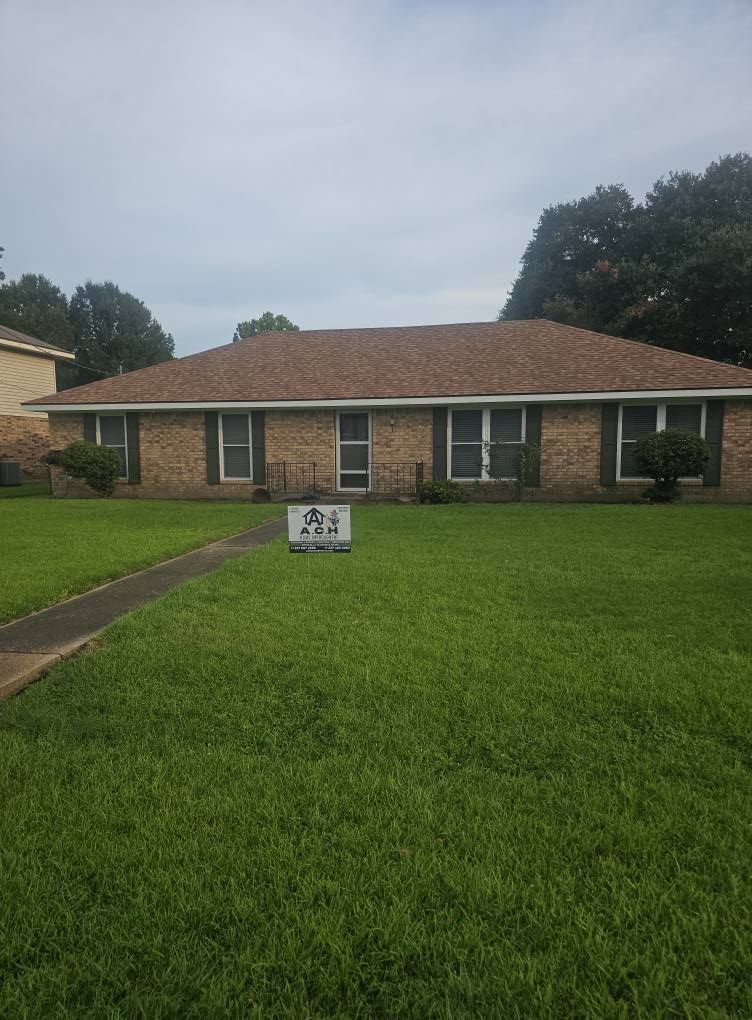 Brick house with brown roof, green lawn, and For Sale sign. Overcast sky.