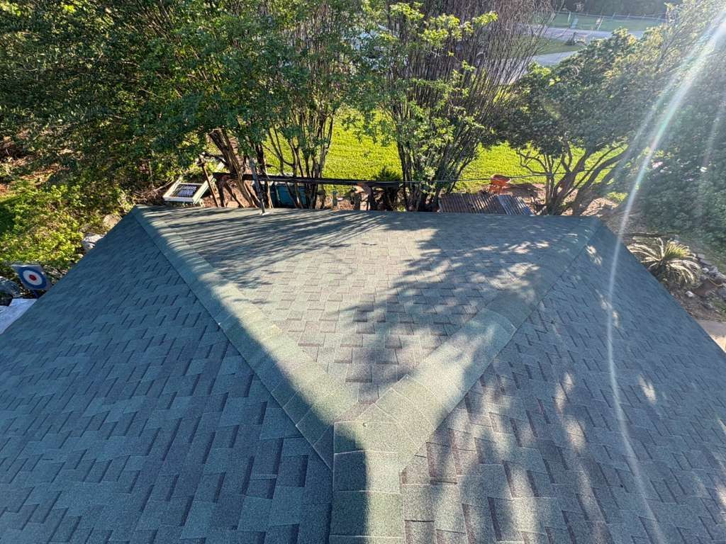 Gray shingled roof with tree shadows and sunlight, viewed from above in a wooded yard
