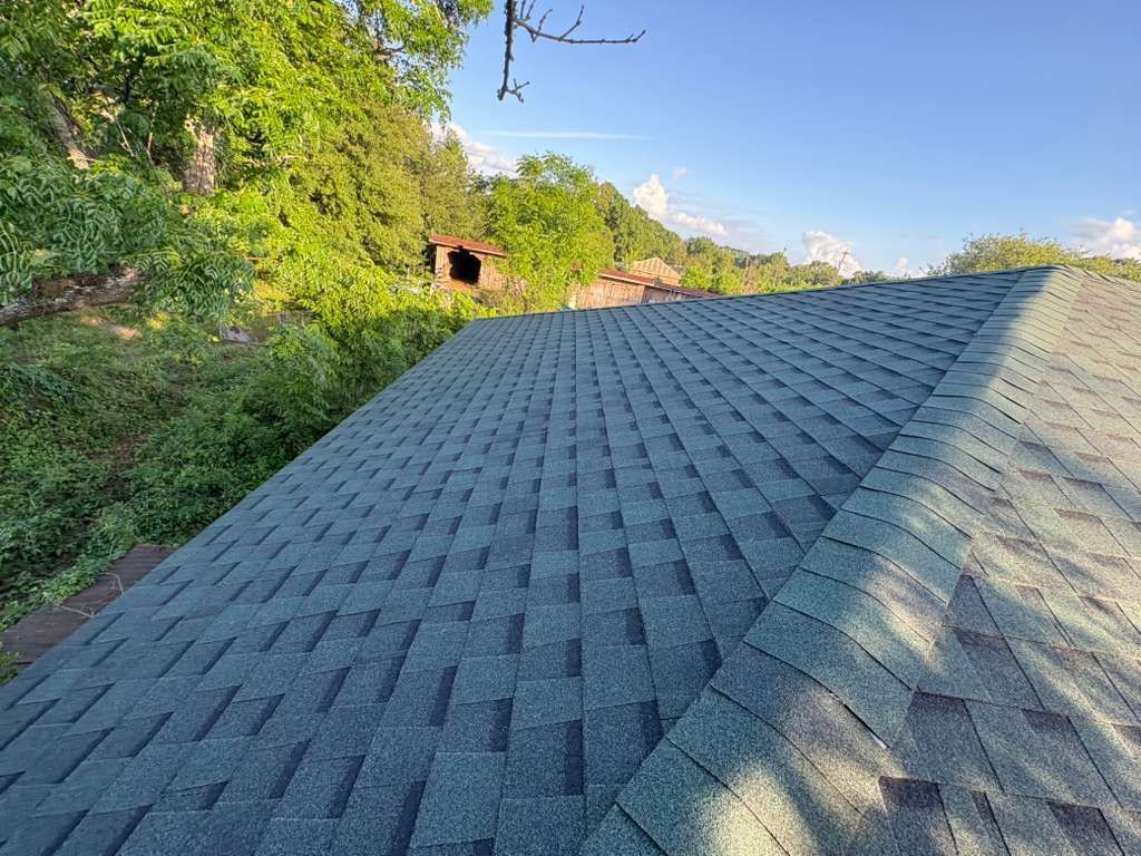 New asphalt roof on a house beside green trees under a blue sky
