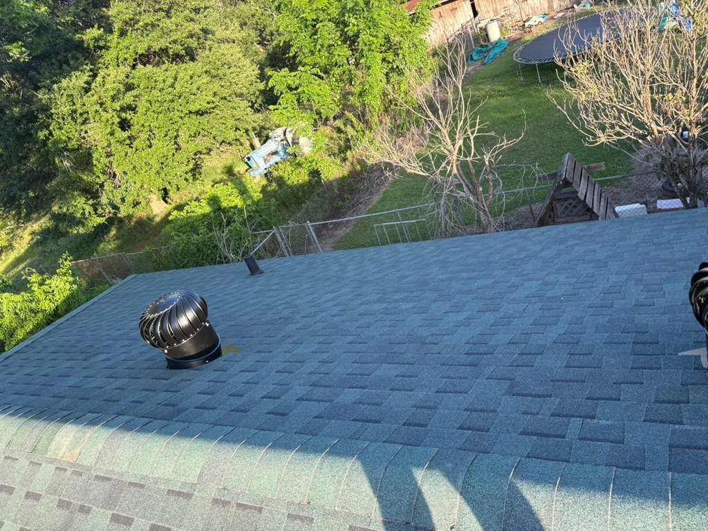 Blue shingled roof with black vents overlooking a green backyard and stairs below