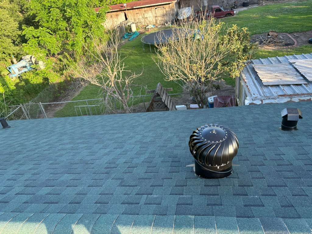 Roof shingles with a black roof vent, overlooking trees and a backyard below.