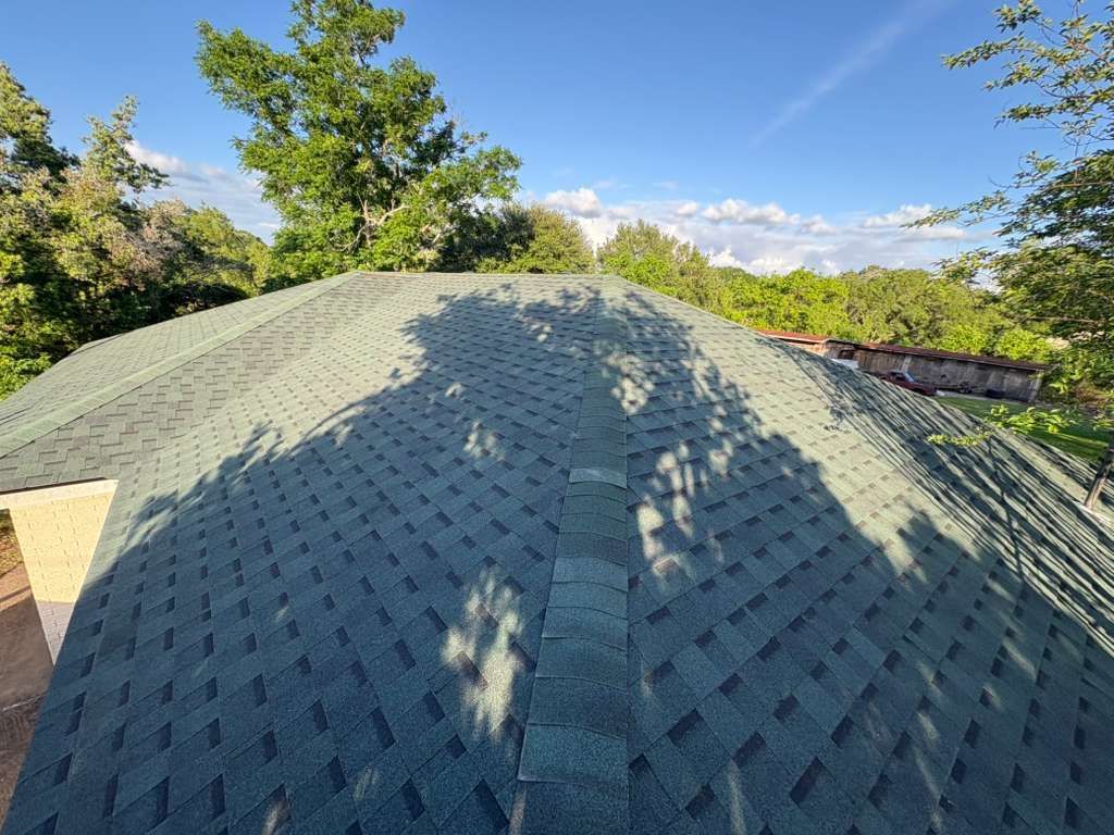 Green shingled roof with tree shadows under a bright blue sky
