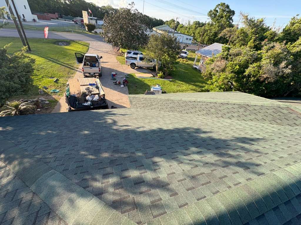 Roof view over a driveway with a parked car, small house, and trees in a sunny neighborhood