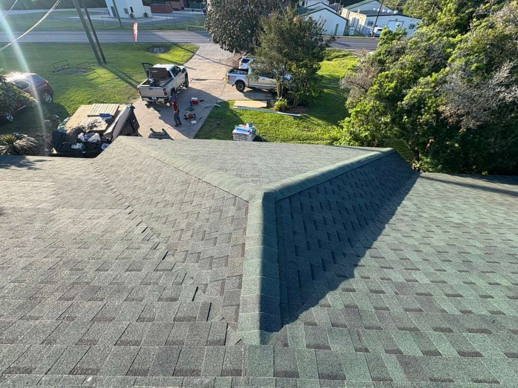 Shingled rooftop with a dormer, overlooking a driveway and trees below