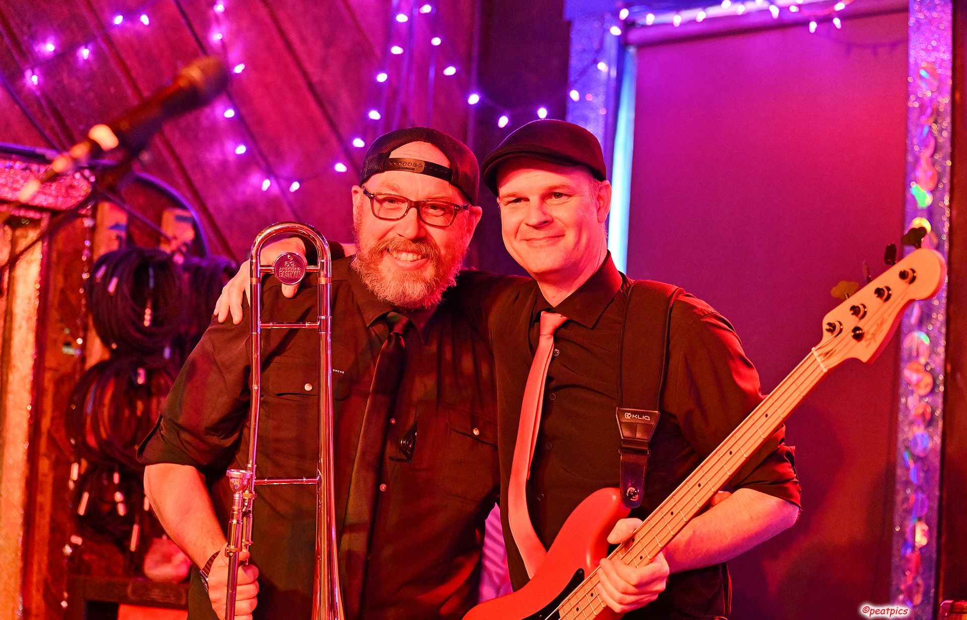 Two men are standing next to each other on a stage holding a bass guitar and a trombone.