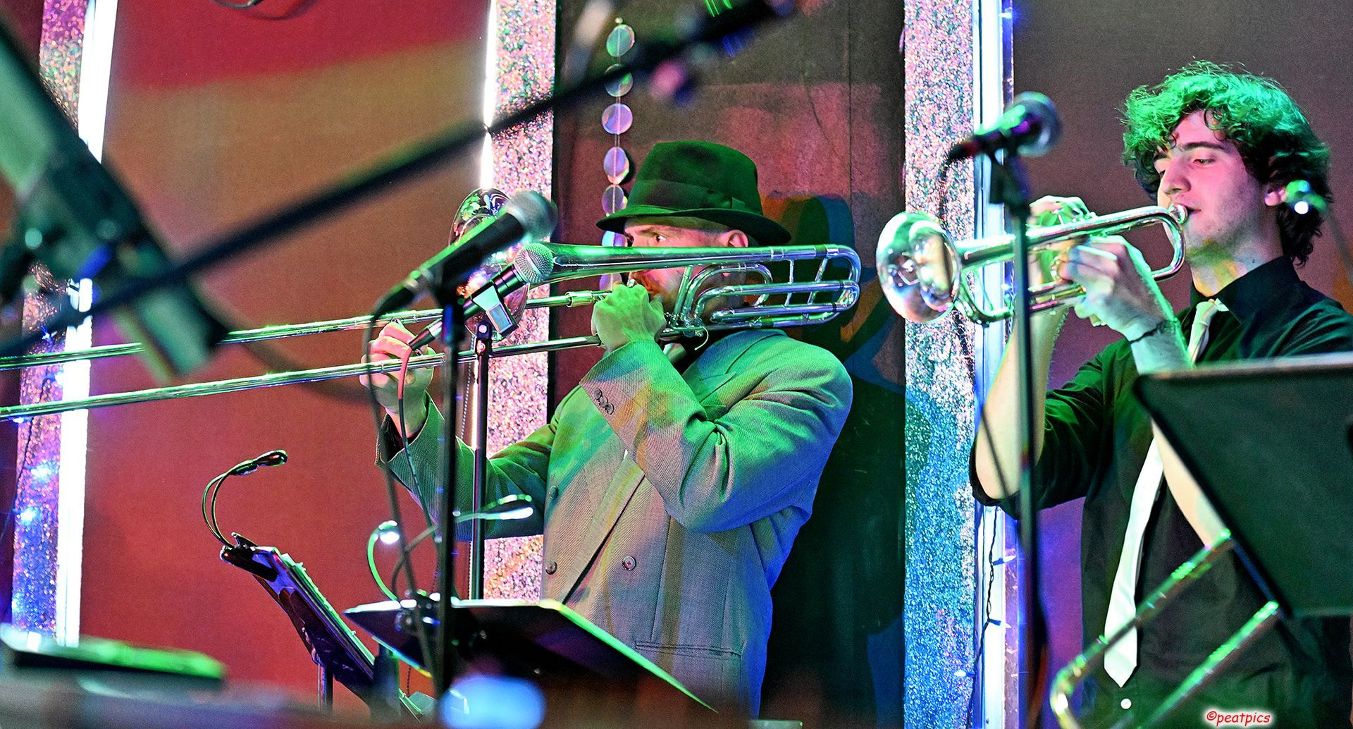 Two men are playing trombones and saxophones on a stage.
