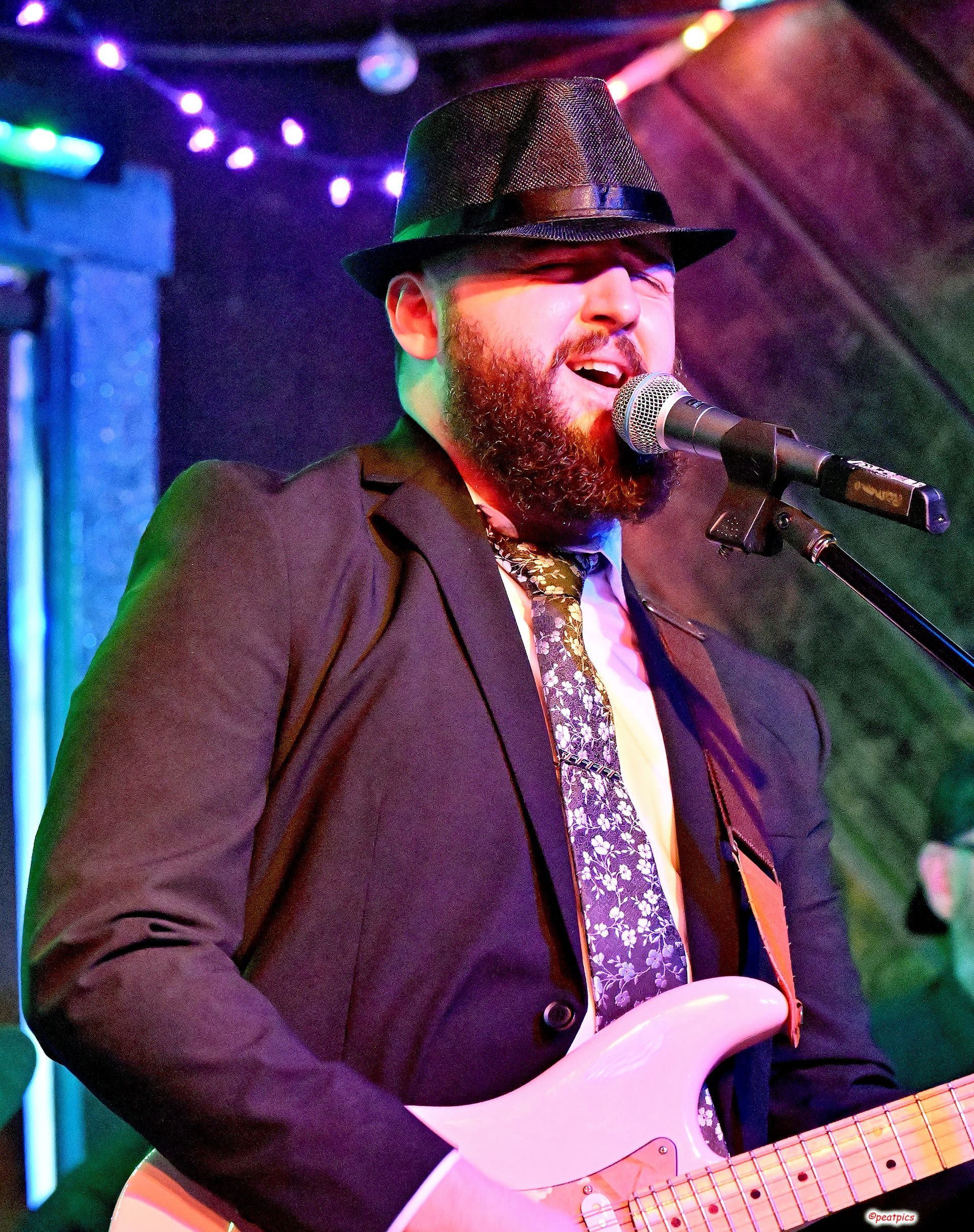 A man with a beard is singing into a microphone while playing a guitar.