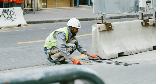 a construction worker is kneeling down on the side of the road .