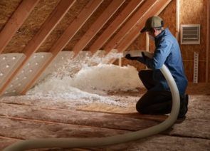 A man is blowing insulation into an attic with a hose.