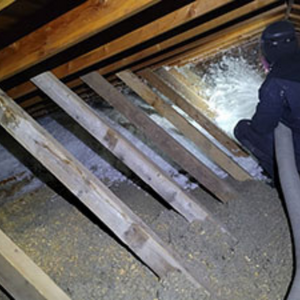 A man is blowing insulation into the attic of a house.