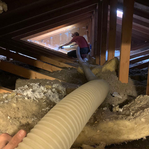 A person is using a hose to remove insulation from an attic