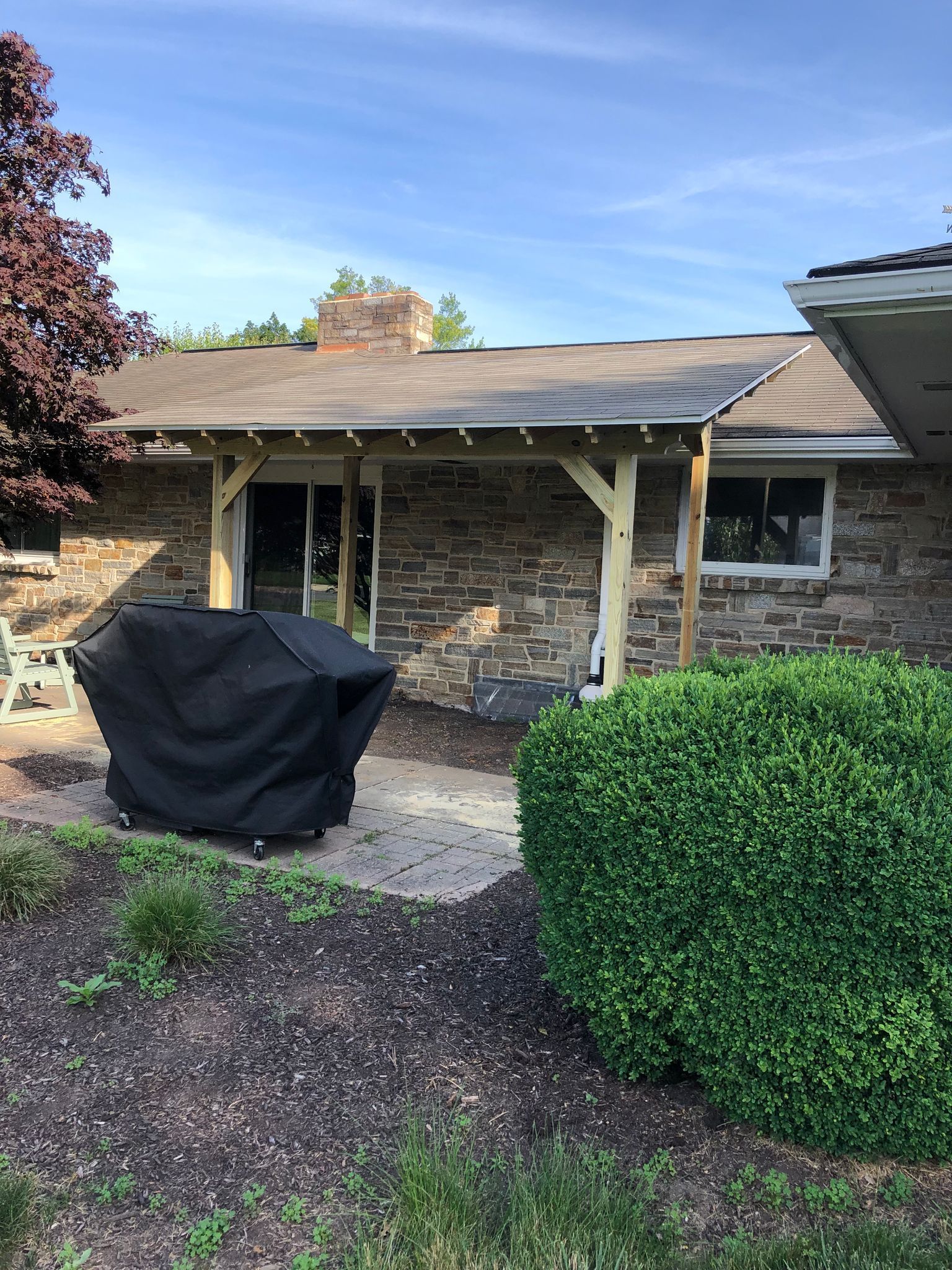 A house with a covered porch and a grill in front of it.