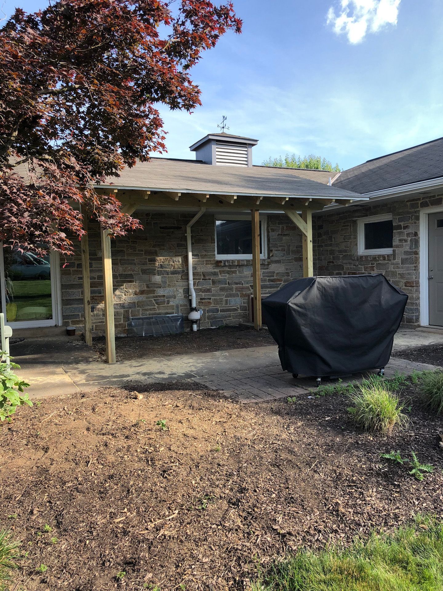 A house with a covered patio and a grill in front of it.