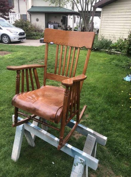 A wooden rocking chair is sitting on a piece of wood in a yard.