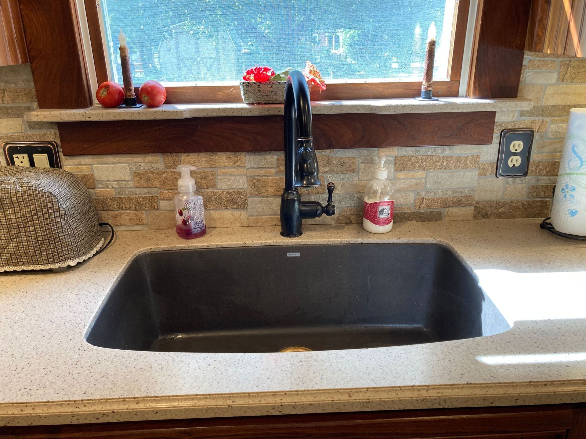 A kitchen sink with a black faucet and a window above it