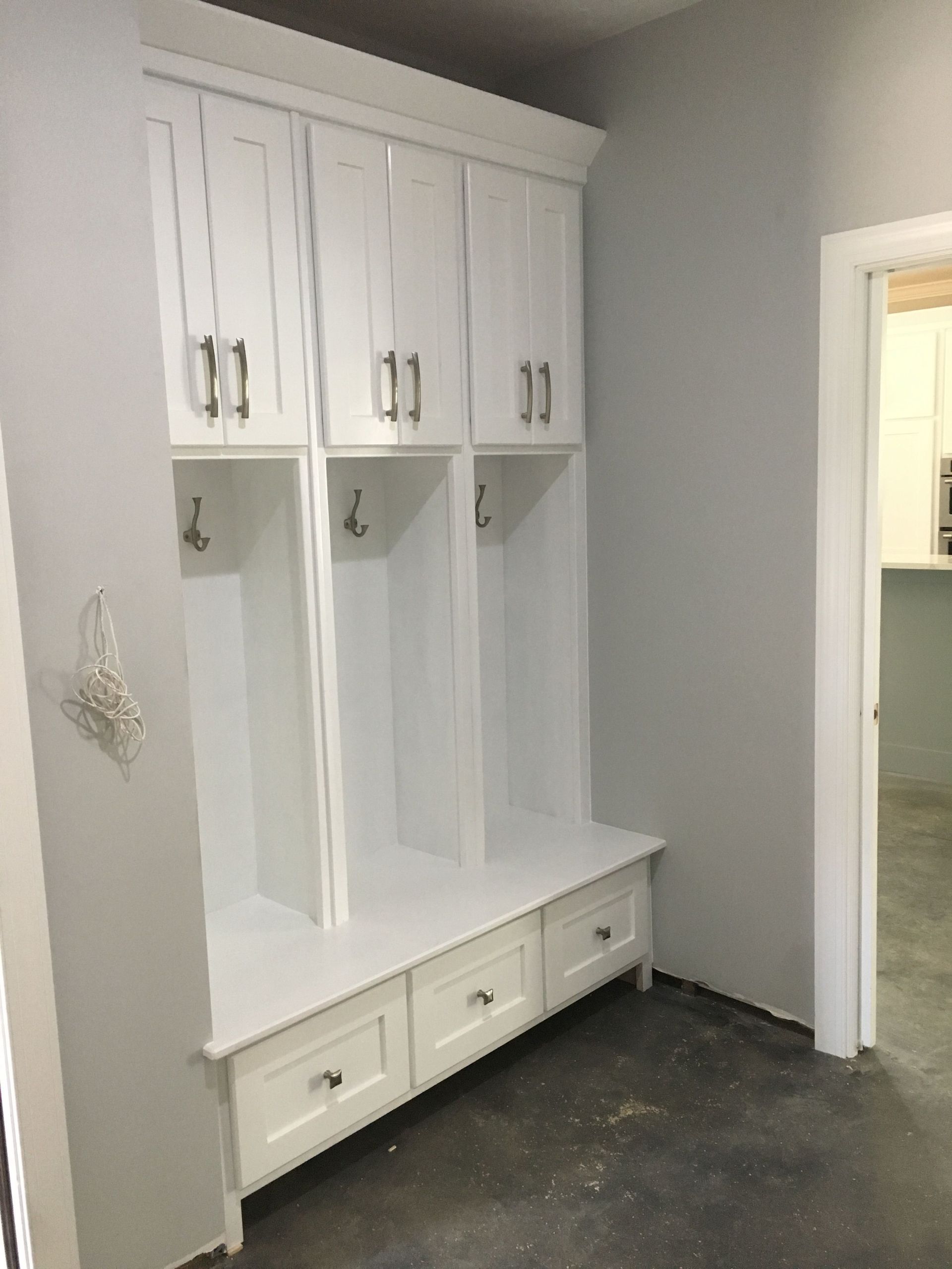 A room with white cabinets , drawers , hooks and a bench.