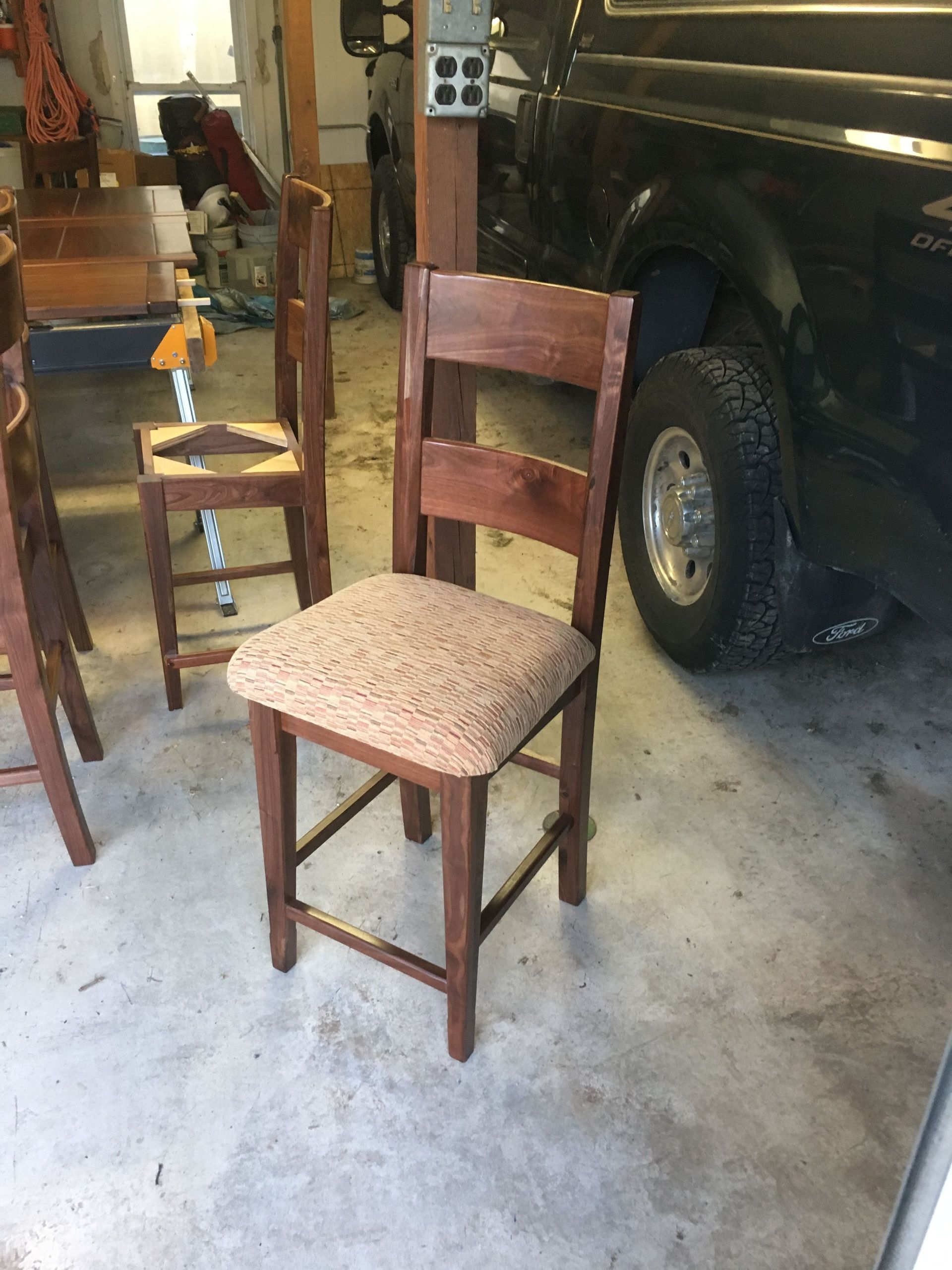 A wooden chair is sitting in a garage next to a black truck.