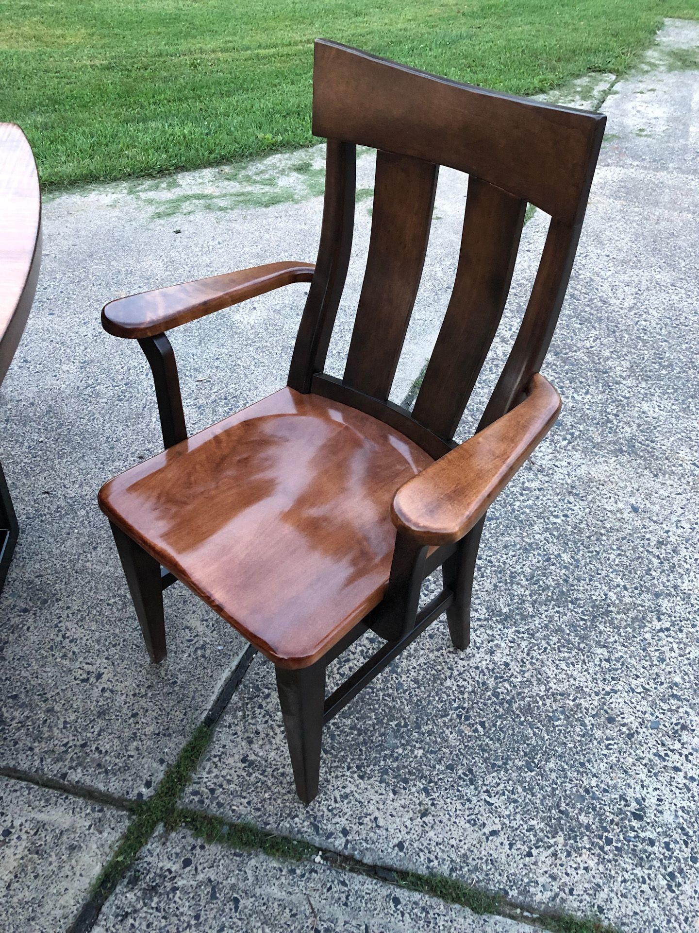 A wooden chair is sitting on a sidewalk next to a table.