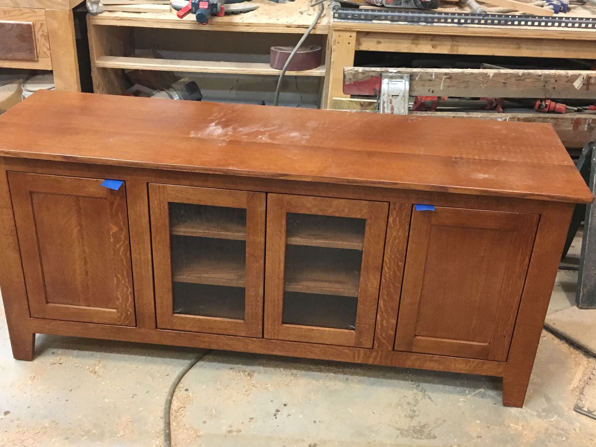 A wooden cabinet with glass doors is sitting on a wooden floor in a workshop.