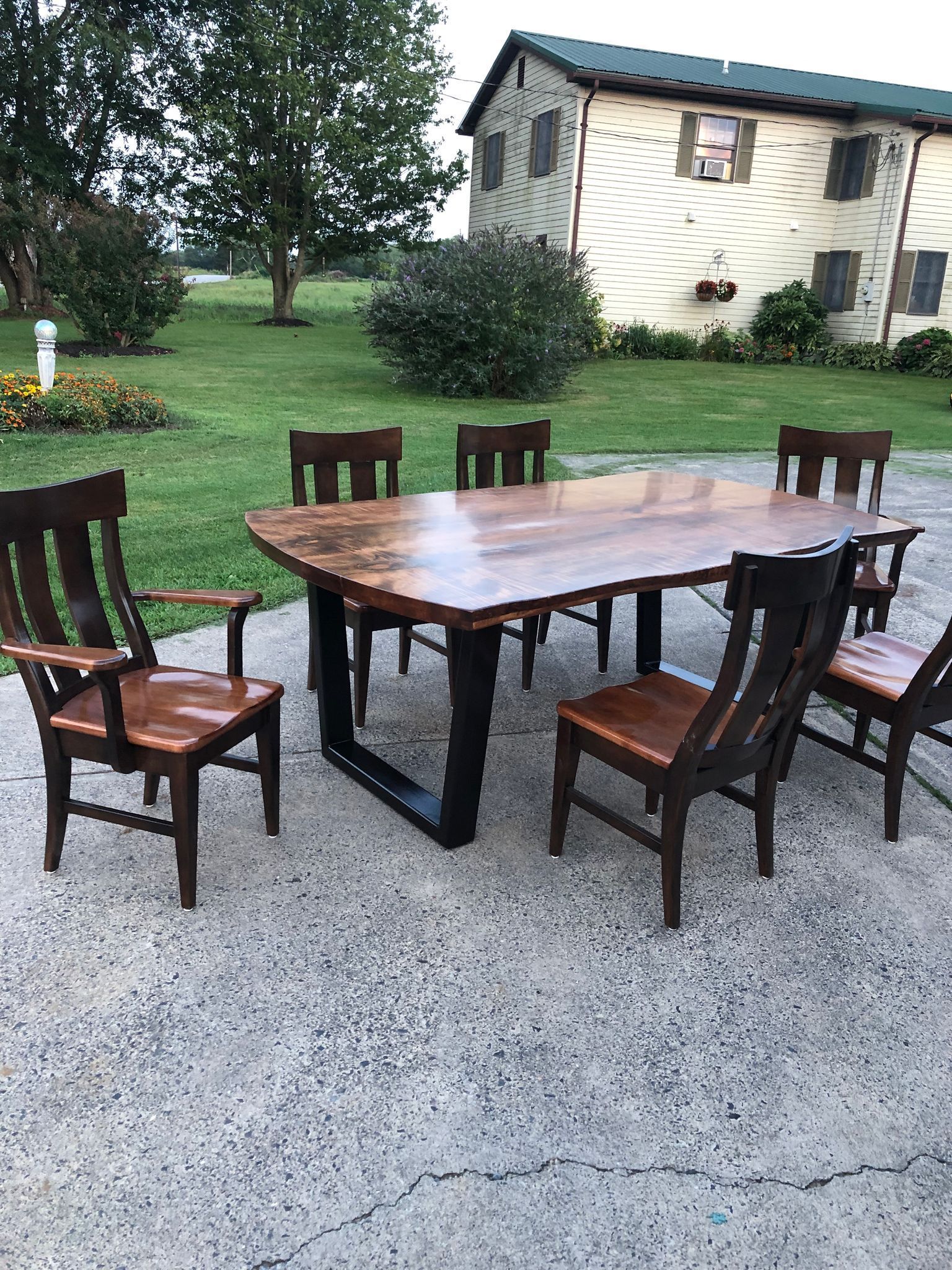 A wooden table and chairs are sitting on a concrete patio in front of a house.