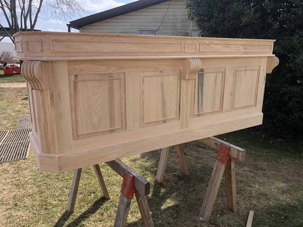 A large wooden box is sitting on top of a wooden stand in a yard.