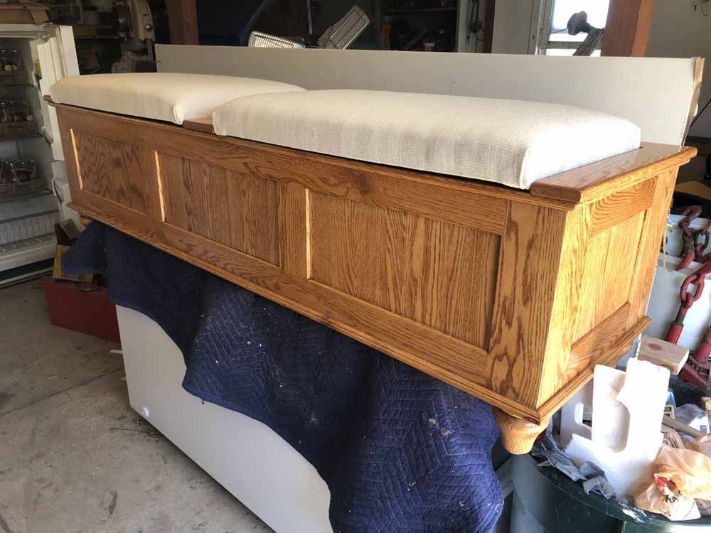 A wooden bench with white cushions is sitting on top of a refrigerator.