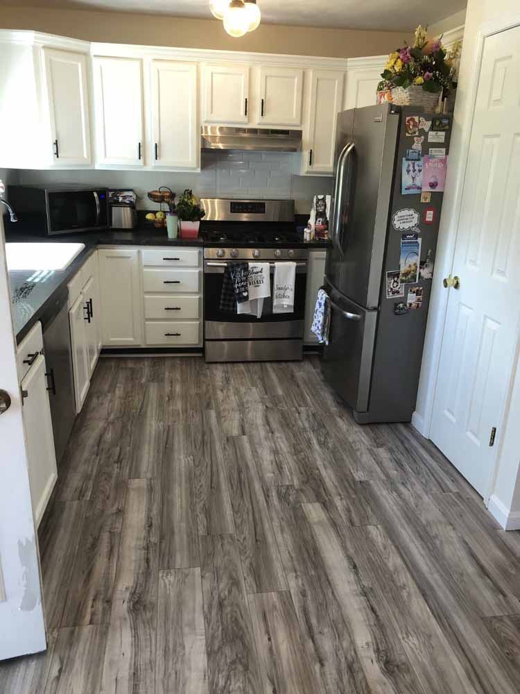 A kitchen with hardwood floors , stainless steel appliances , and white cabinets.