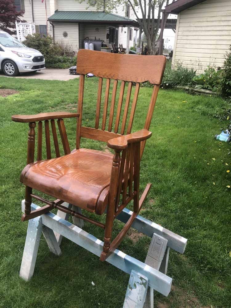 A wooden rocking chair is sitting on top of a wooden trestle in a yard.