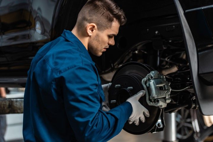 Mechanic in blue coveralls inspecting a car brake assembly in a workshop