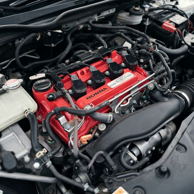 Close-up of a car engine bay with a bright red valve cover and surrounding hoses
