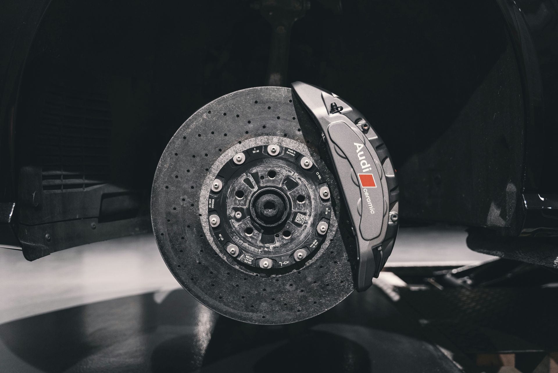 Close-up of a race car wheel and brake assembly on a dark stage, with a carbon-fiber rim and tire.