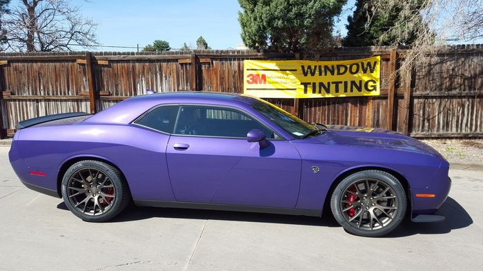 A purple dodge challenger is parked in front of a window tinting sign.