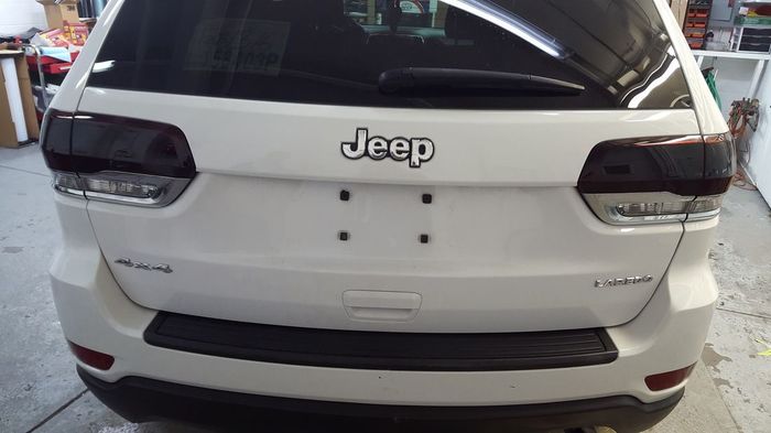 A white jeep with black tail lights is parked in a garage.