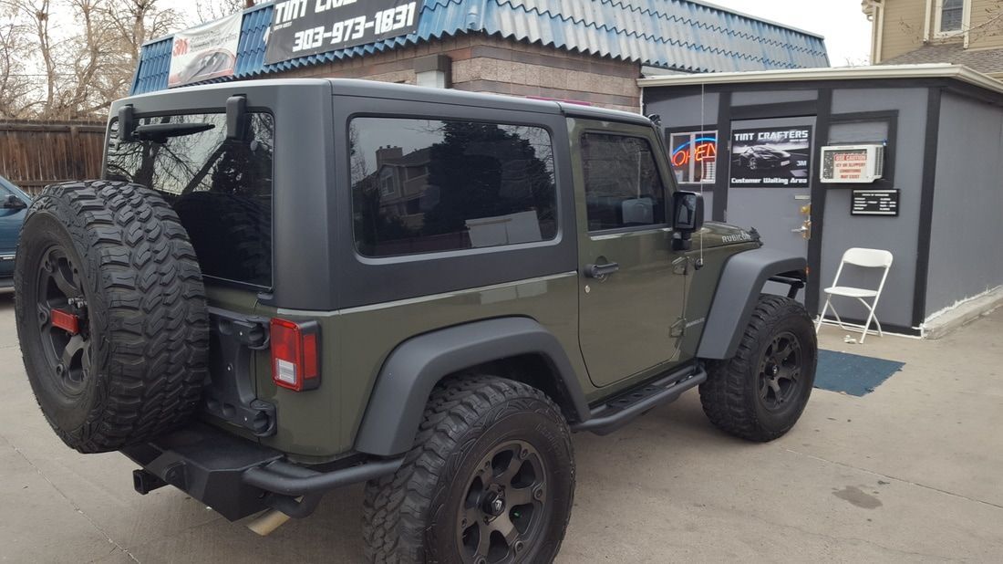 A green jeep is parked in front of a building.