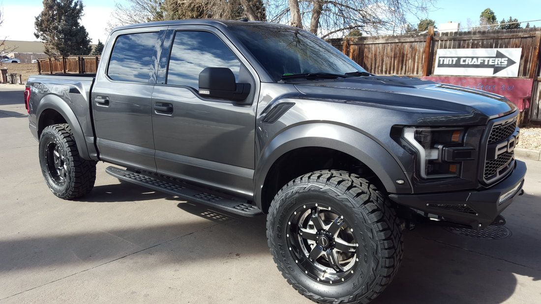 A gray ford raptor is parked on the side of the road.