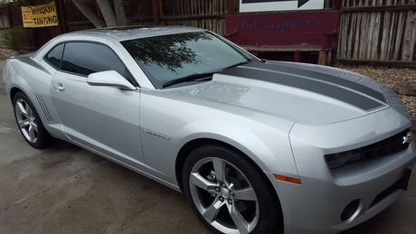 A silver car with a black stripe on the hood is parked in a parking lot.