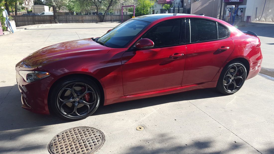 A red car is parked on the side of the road next to a manhole cover.
