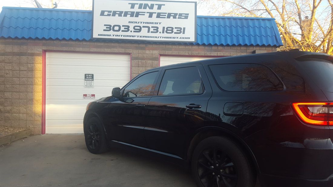 A black car is parked in front of a building that says tint drafters.
