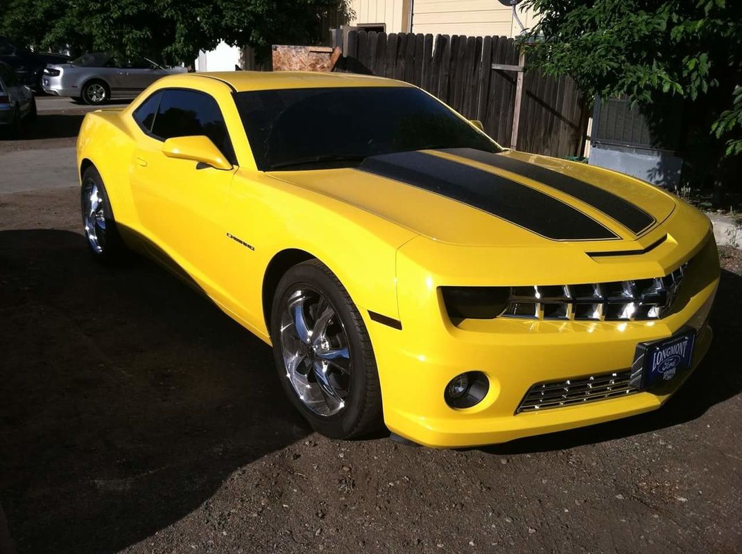 A yellow car with black stripes is parked in a driveway