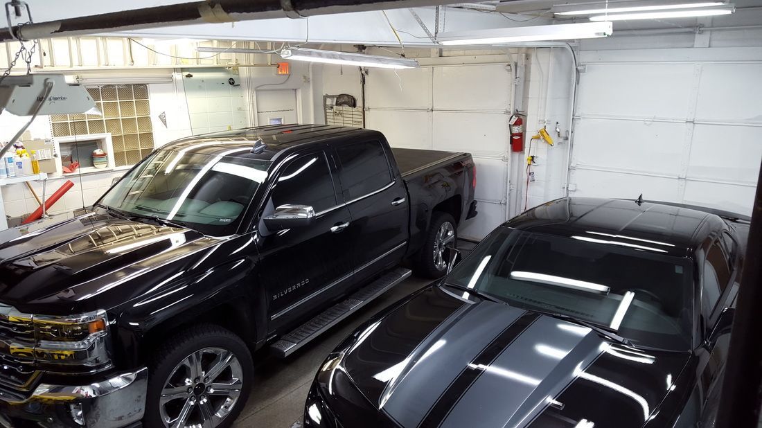 Two black cars are parked in a garage next to a truck.