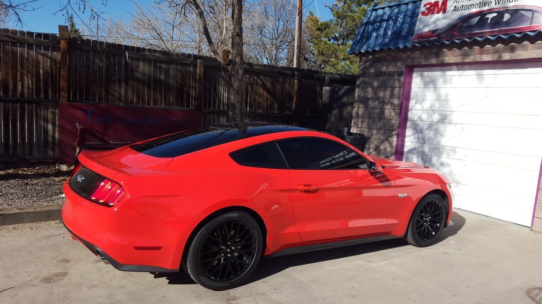 A red mustang is parked in front of a garage.