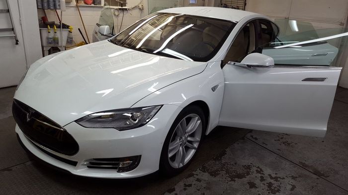 A white tesla model s is parked in a garage with its doors open.