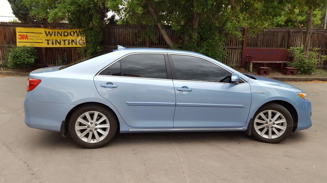 A blue car is parked in front of a window tinting sign.